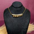 Close-up view of the Gleaming Bead Curve Bar Necklace highlighting the crystal curve bar and hanging gold beads on a black bust.