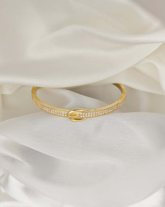 Elegant gold-tone crystal bracelet with infinity-inspired design displayed on white satin fabric