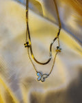 Elegant gold layered necklace featuring a pearl-inspired butterfly pendant and delicate butterfly charms displayed on luxurious satin fabric