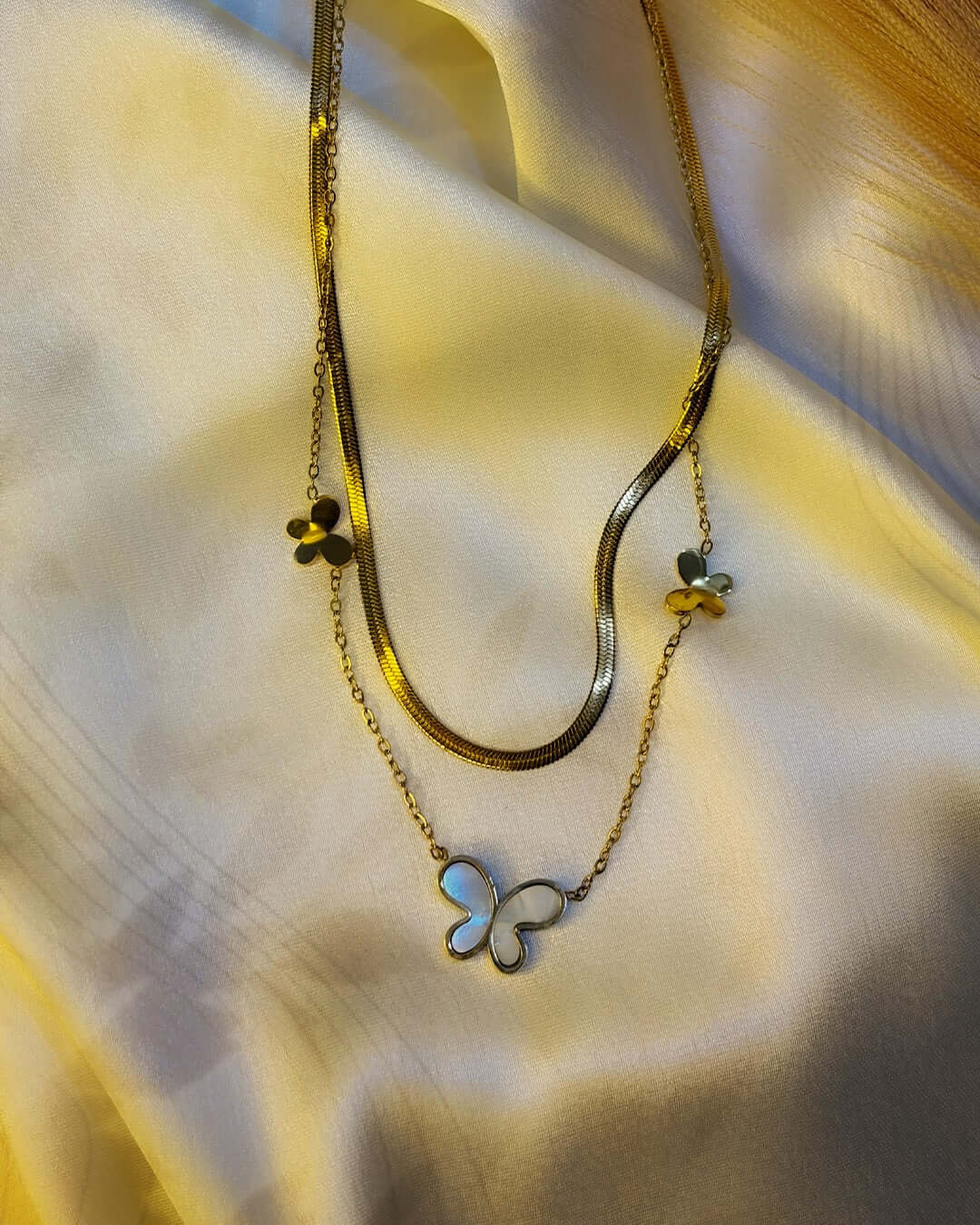 Elegant gold layered necklace featuring a pearl-inspired butterfly pendant and delicate butterfly charms displayed on luxurious satin fabric