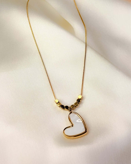 Close-up view of a white heart pendant necklace with gold-tone detailing on a soft satin fabric background