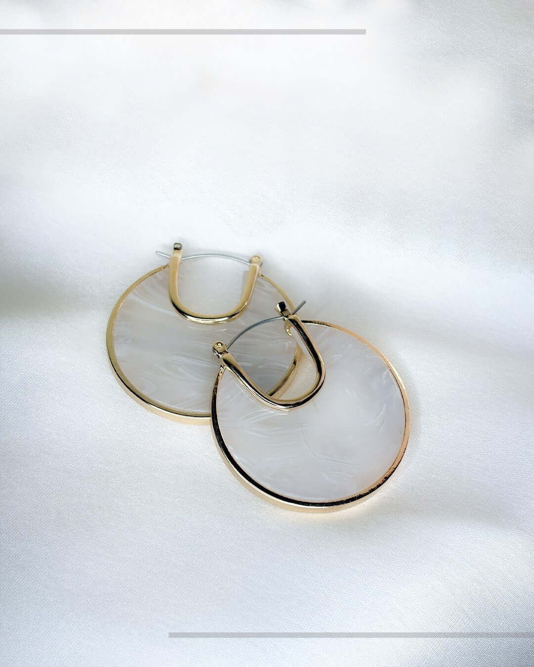 Ivory marble statement hoop earrings with gold-tone detailing displayed on a soft white fabric background