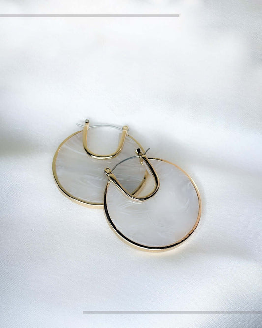 Ivory marble statement hoop earrings with gold-tone detailing displayed on a soft white fabric background