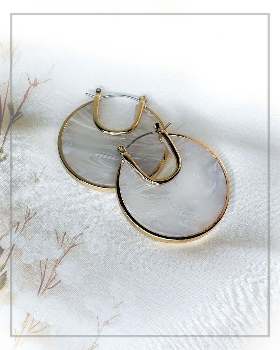 Elegant ivory marble hoop earrings with gold-tone frame styled on a luxury fabric backdrop