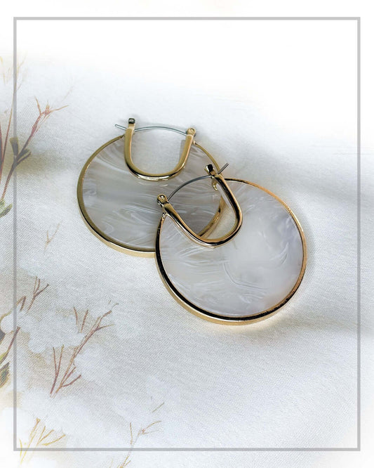 Elegant ivory marble hoop earrings with gold-tone frame styled on a luxury fabric backdrop