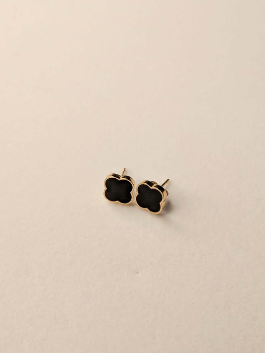 Black clover-shaped stud earrings with a gold-tone border displayed on a soft beige background