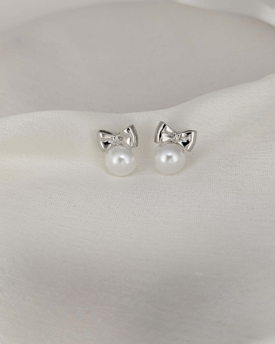 Close-up view of elegant silver bow pearl stud earrings for women
